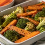 A tray of roasted broccoli and carrots, crispy and caramelized, garnished with fresh herbs.